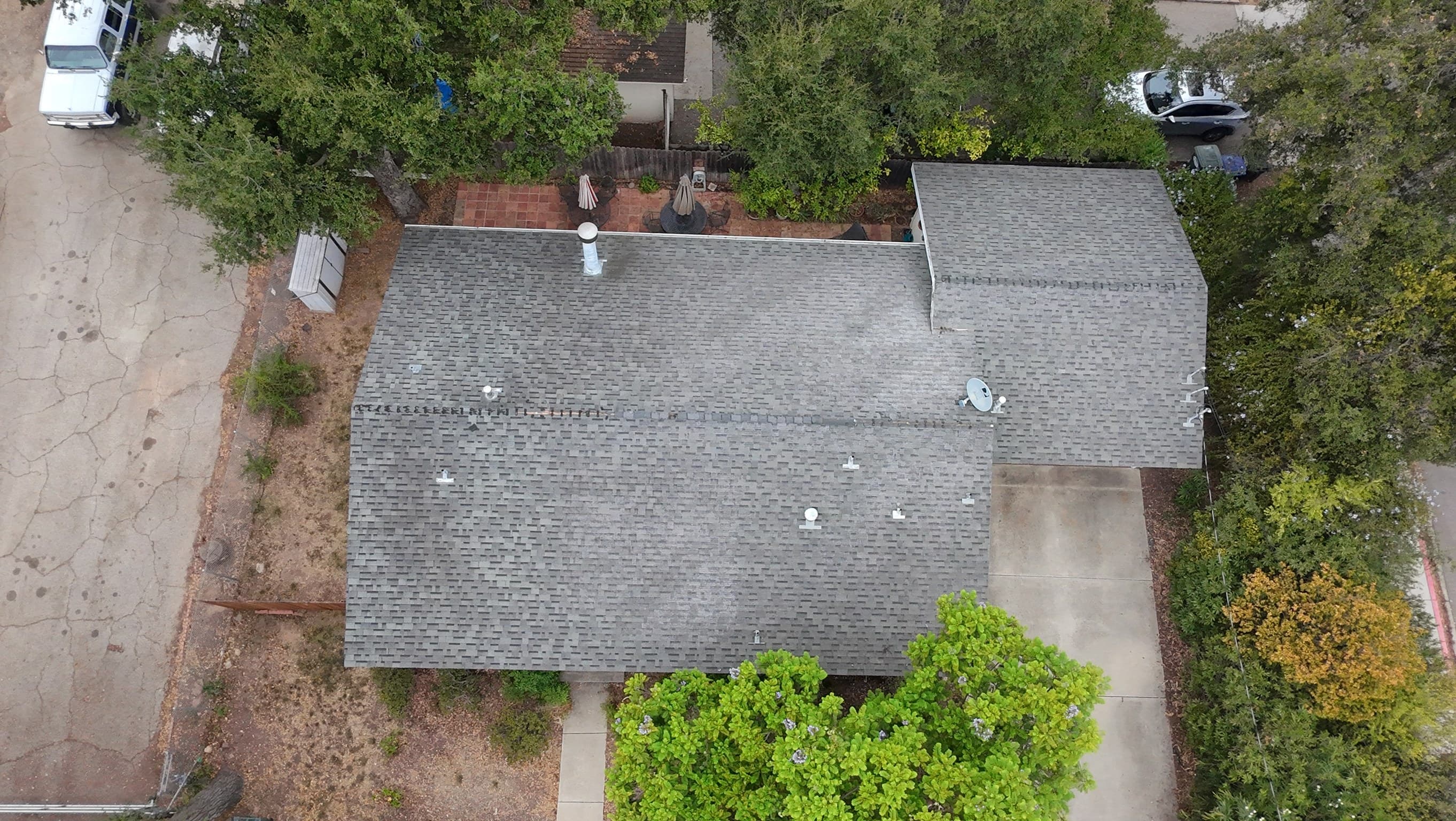 Aerial view of the same house before the job, its composition roof an even weathered gray, oaks and a cracked concrete drive around it