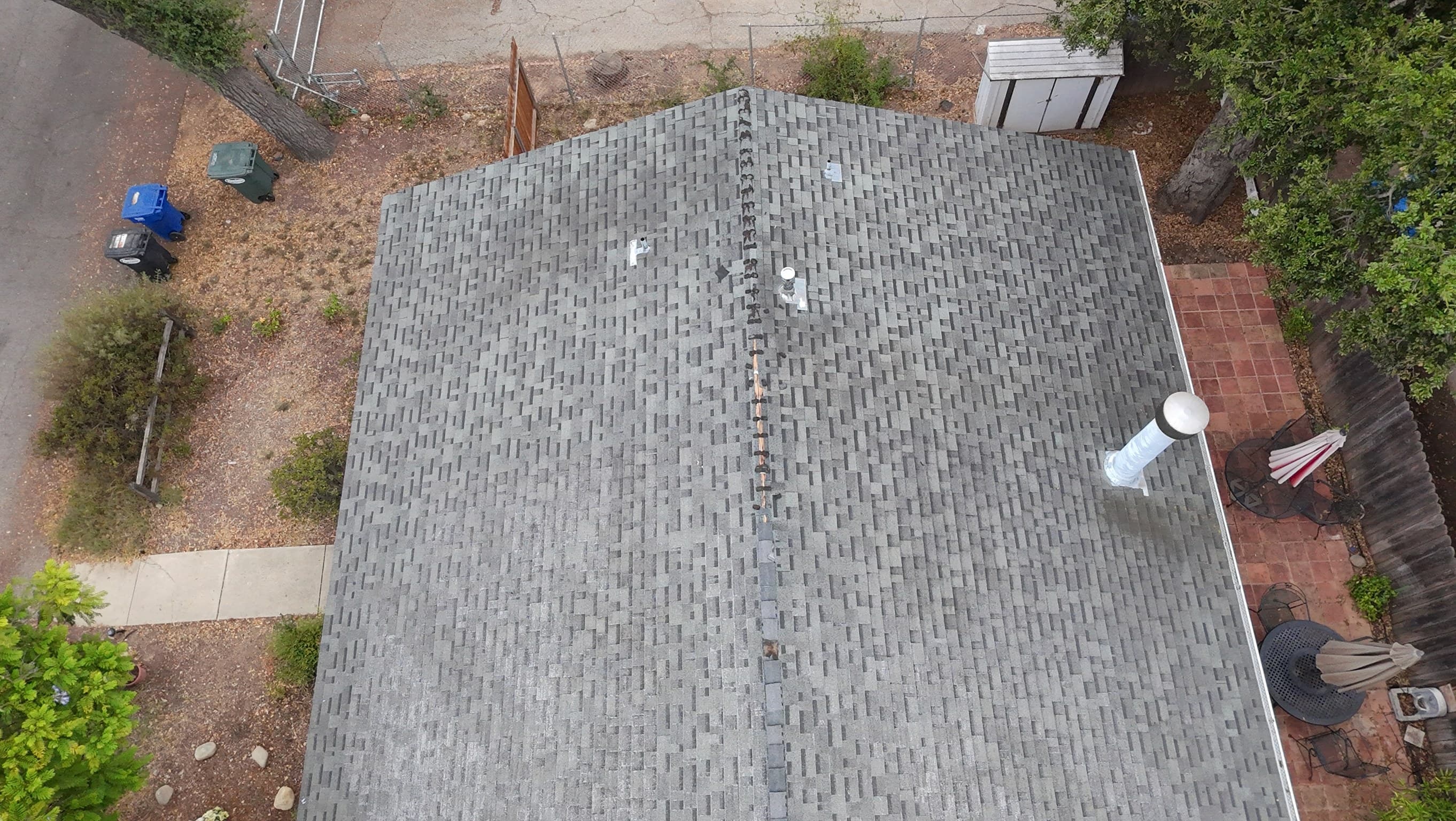Looking straight down at the gray roof, where a tall flue beside the eave has been wrapped in plastic and taped ahead of spraying