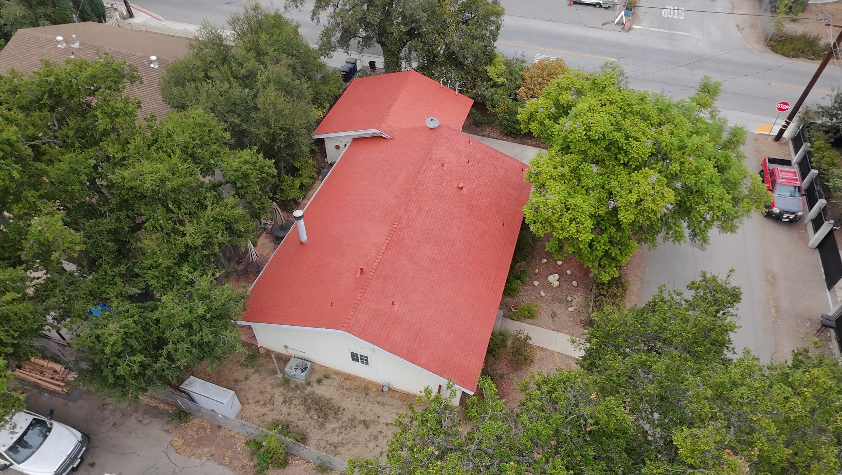 Aerial view of a single-story house whose composition roof is finished in terracotta Roof Coat, oaks and a quiet street corner around it