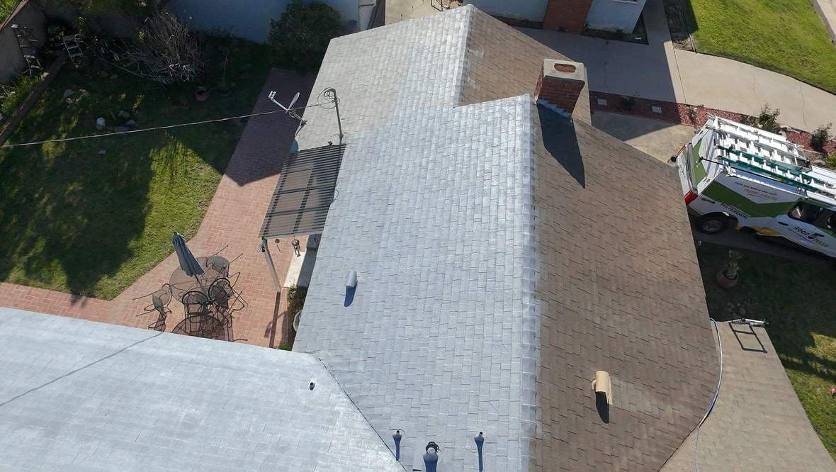Residential roof mid-coating. Light gray coated planes next to brown uncoated composition shingle.