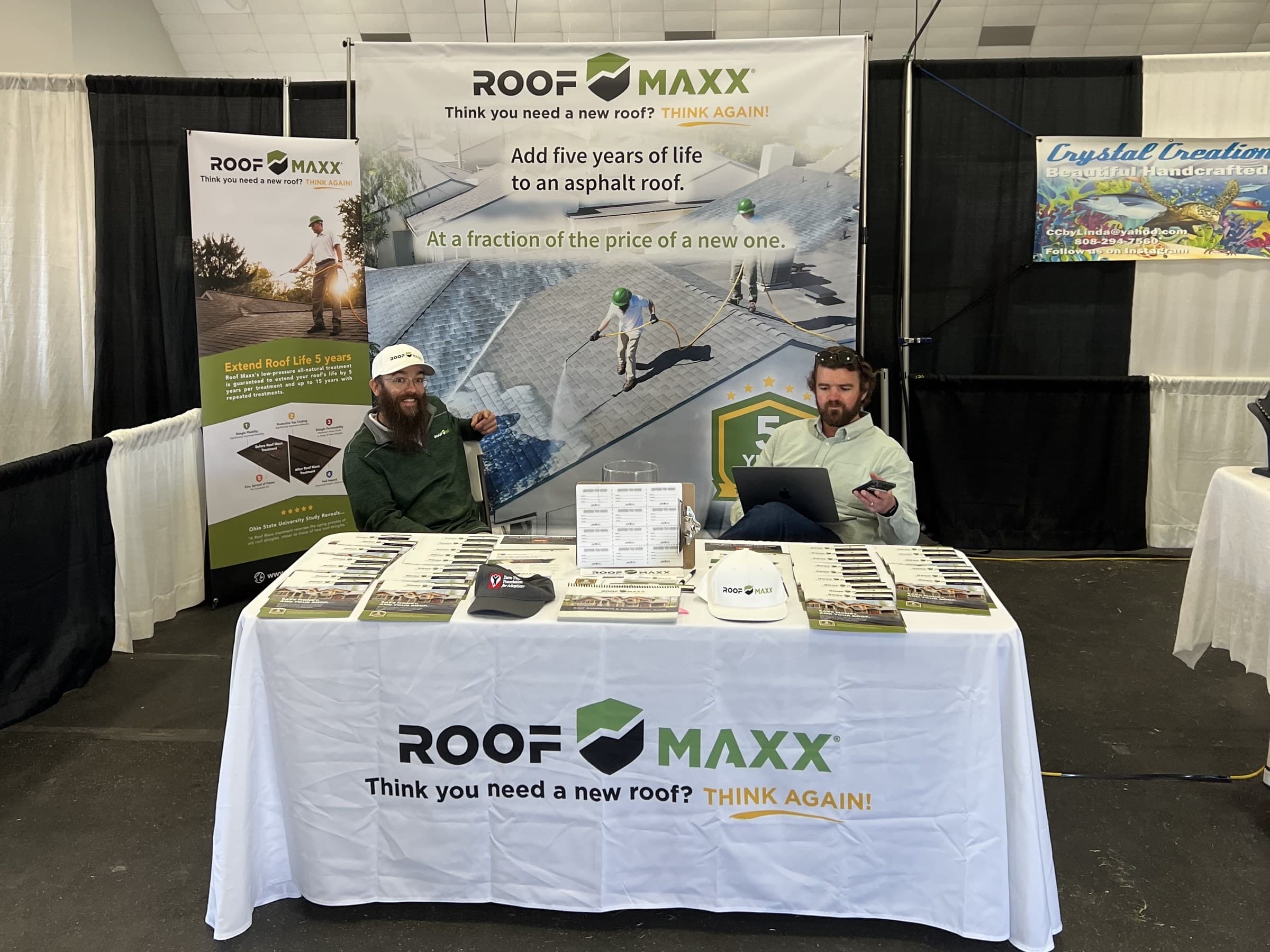 The Roof Maxx booth at a trade show: banners, a branded table of handouts, and two of our team behind it