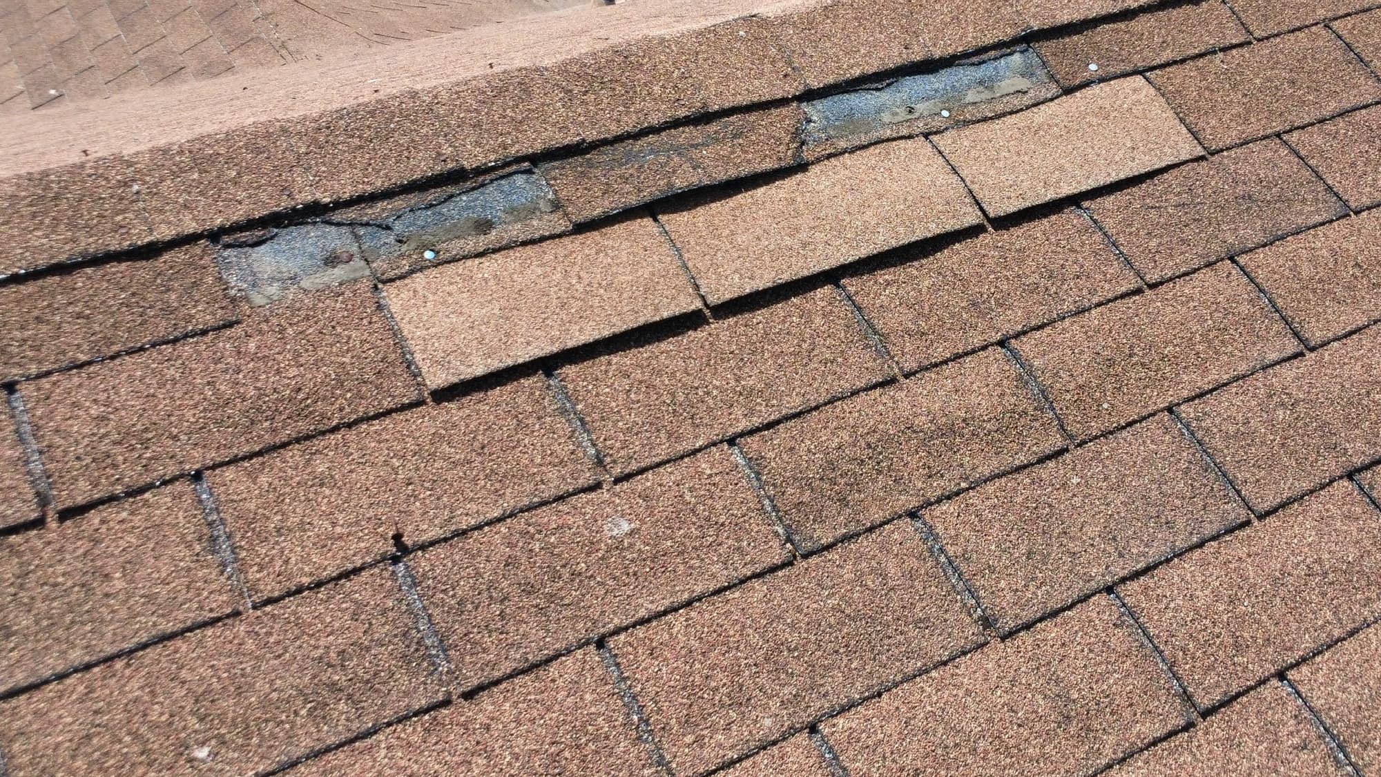 Two shingle tabs missing from the course just below a Simi Valley ridge, leaving the gray headlap of the course beneath exposed, with a nail head visible in the left gap.