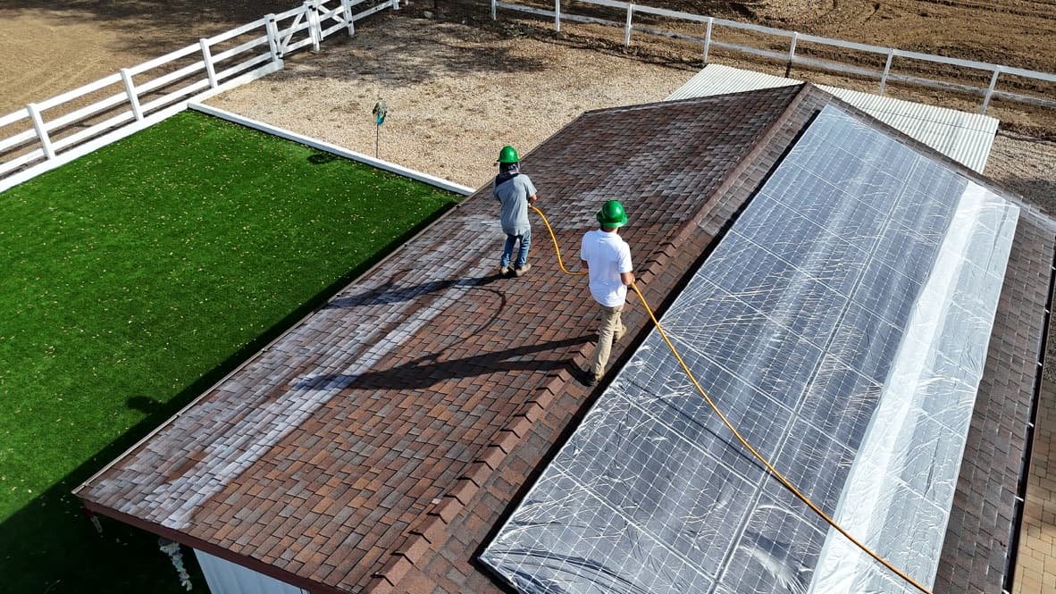 Aerial view along an estate ridge, two crew members walking the slope with a hose while the solar array beside them stays covered in protective sheeting