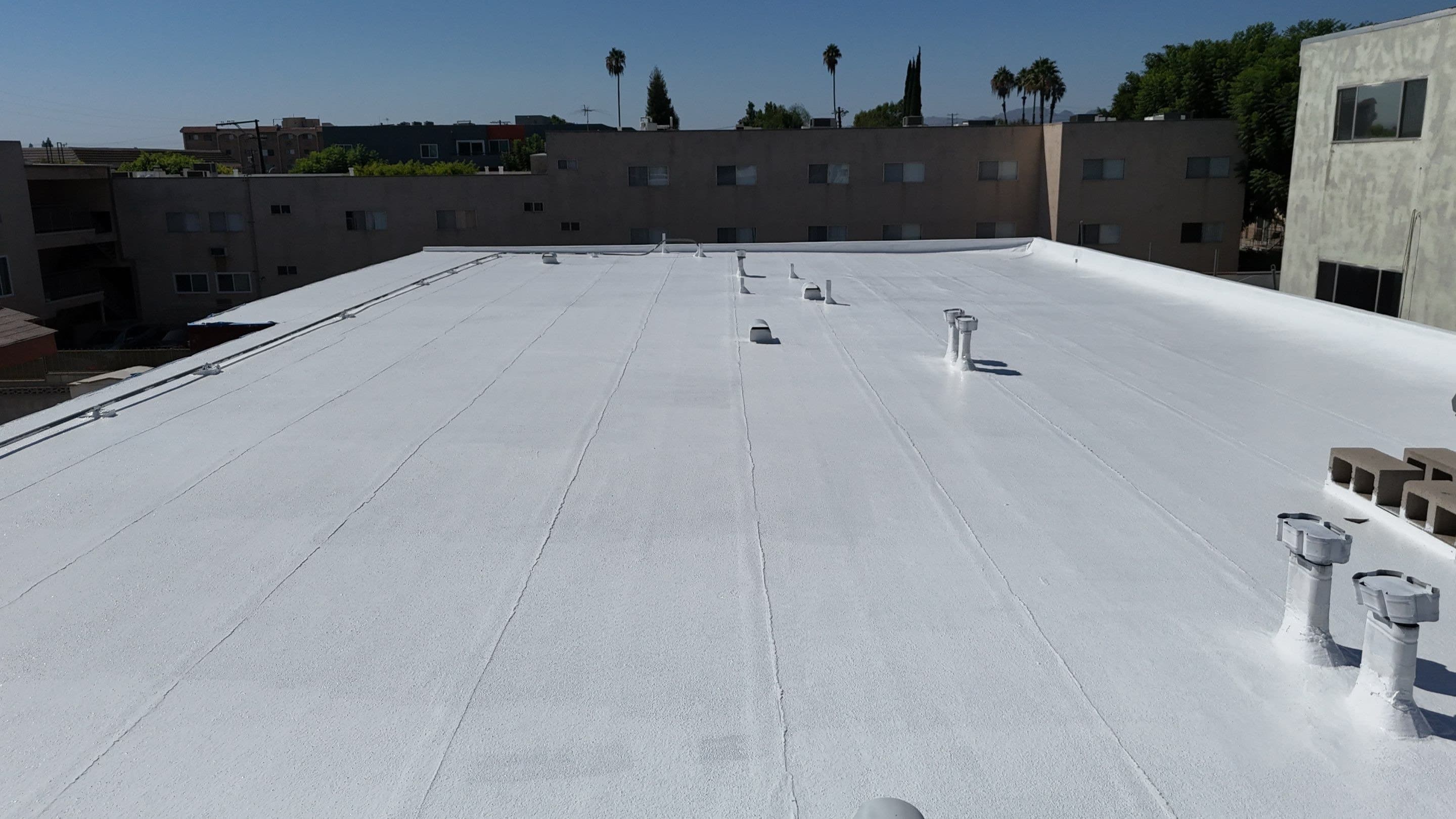 The finished white silicone field on a flat Northridge apartment roof, seen from above.