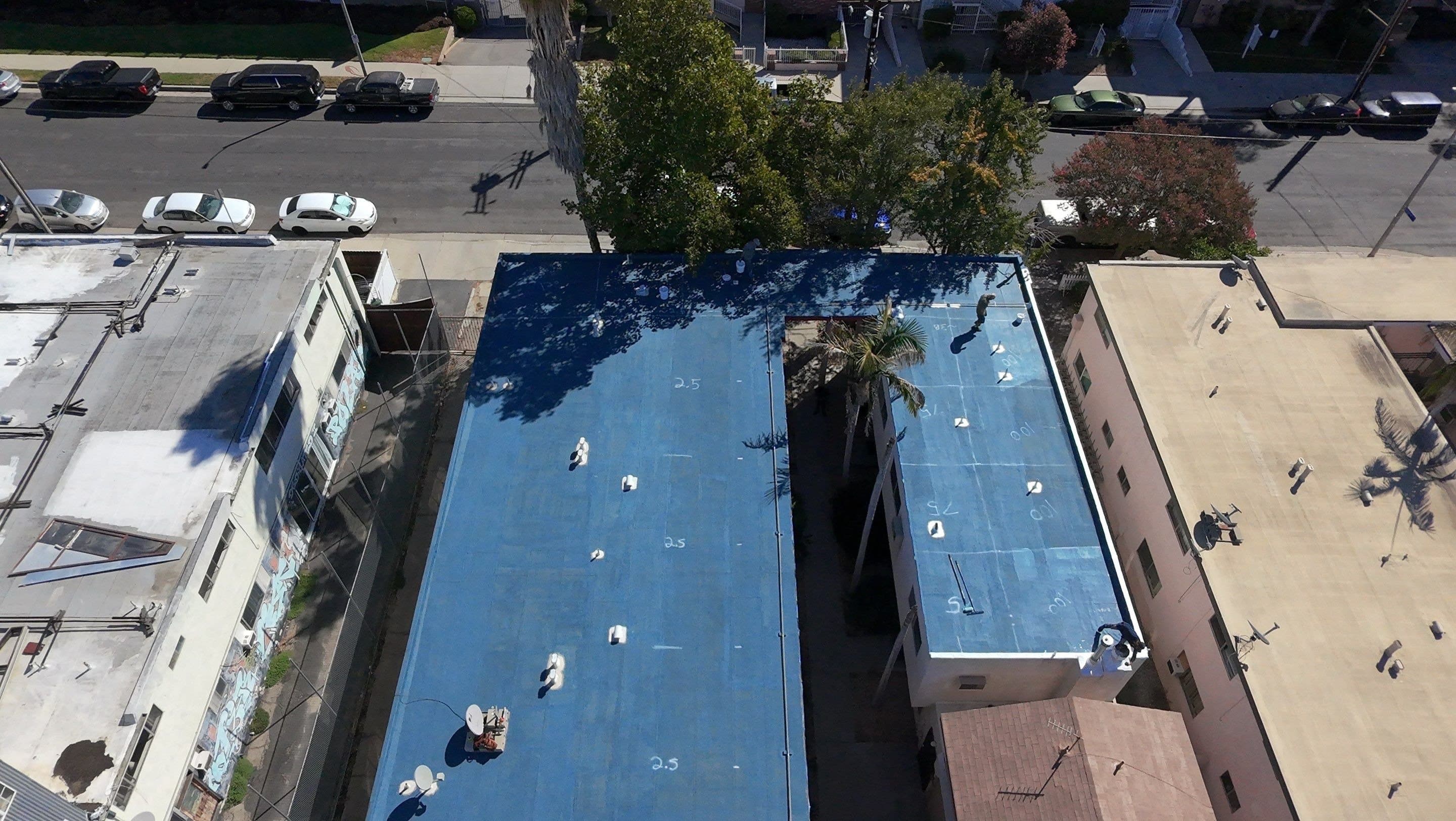 Aerial view of blue base coat on the flat roof, with the detached shingle building already coated.
