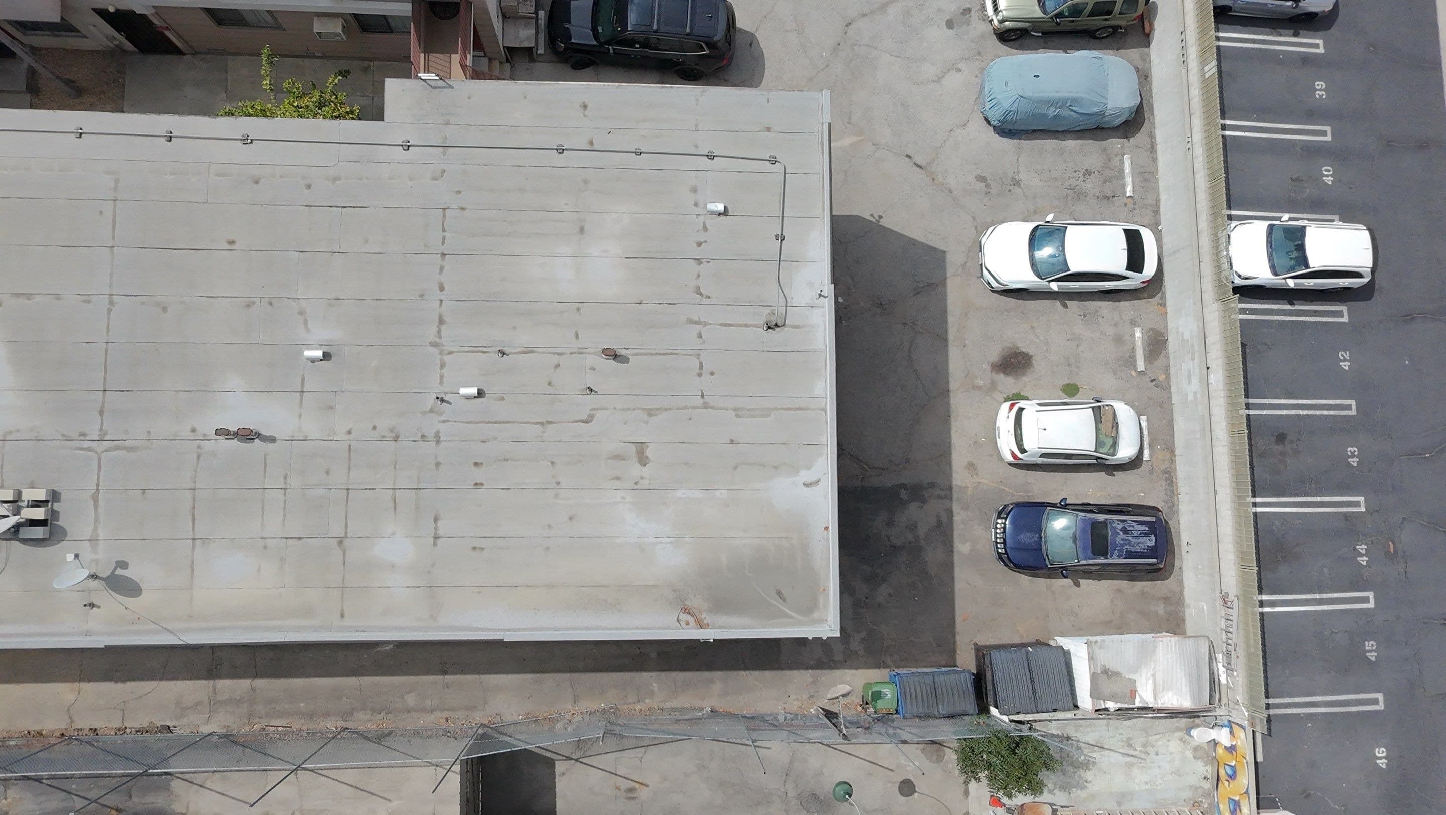 Aerial view of a worn gray flat roof beside an apartment parking lot, before any coating.