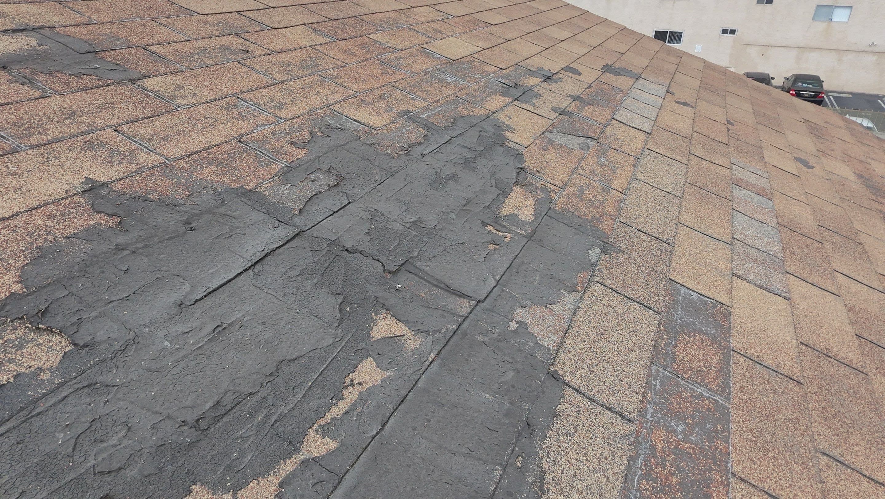 Dark mastic smeared across weathered shingles on the detached building.