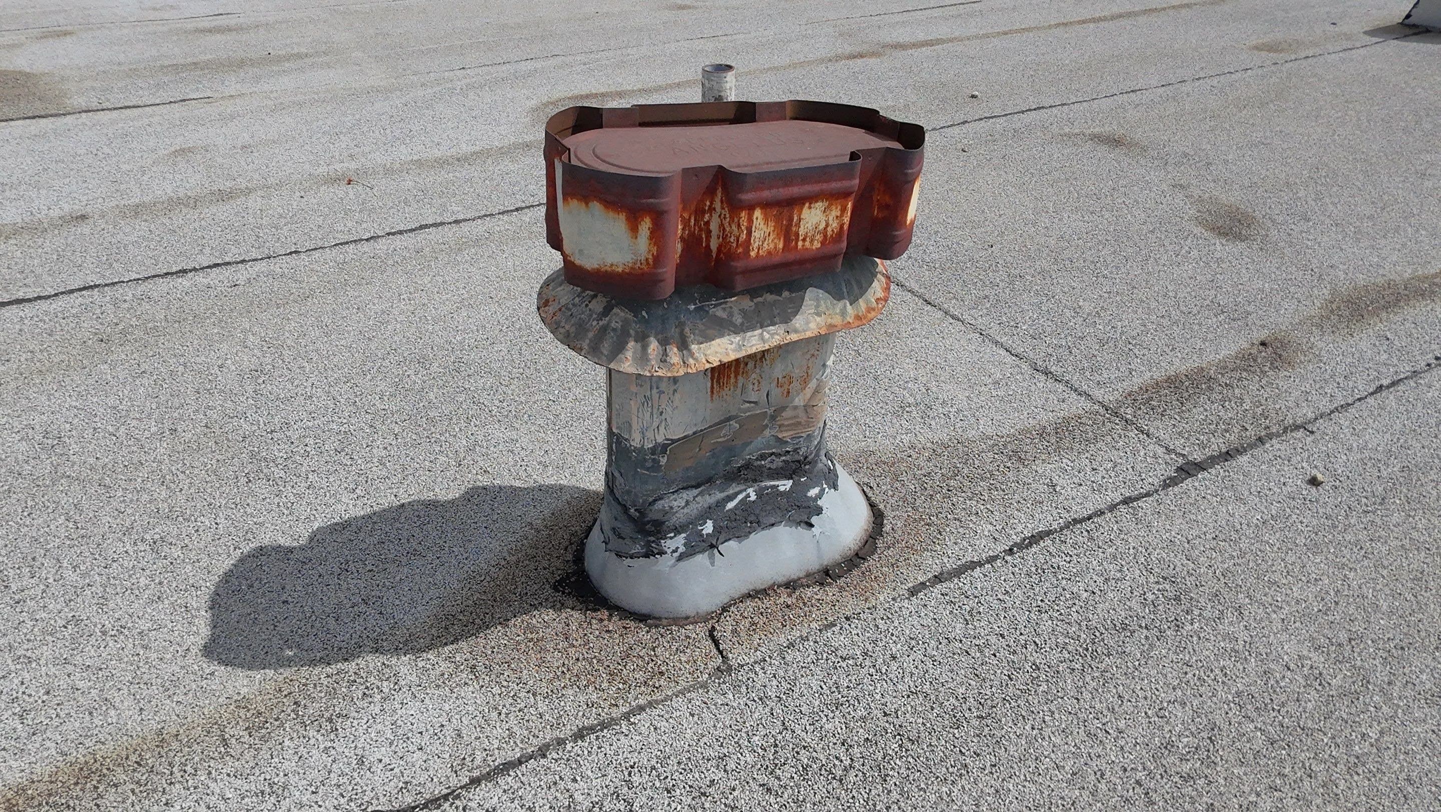 A corroded metal vent curb standing on the worn cap sheet.