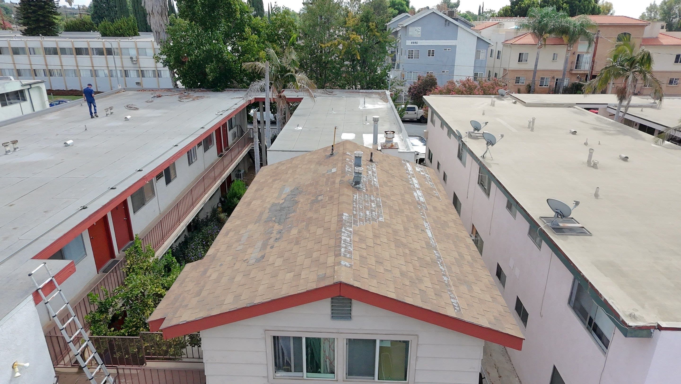 Aerial view of a small detached building whose shingle roof is patched, beside the flat roof.