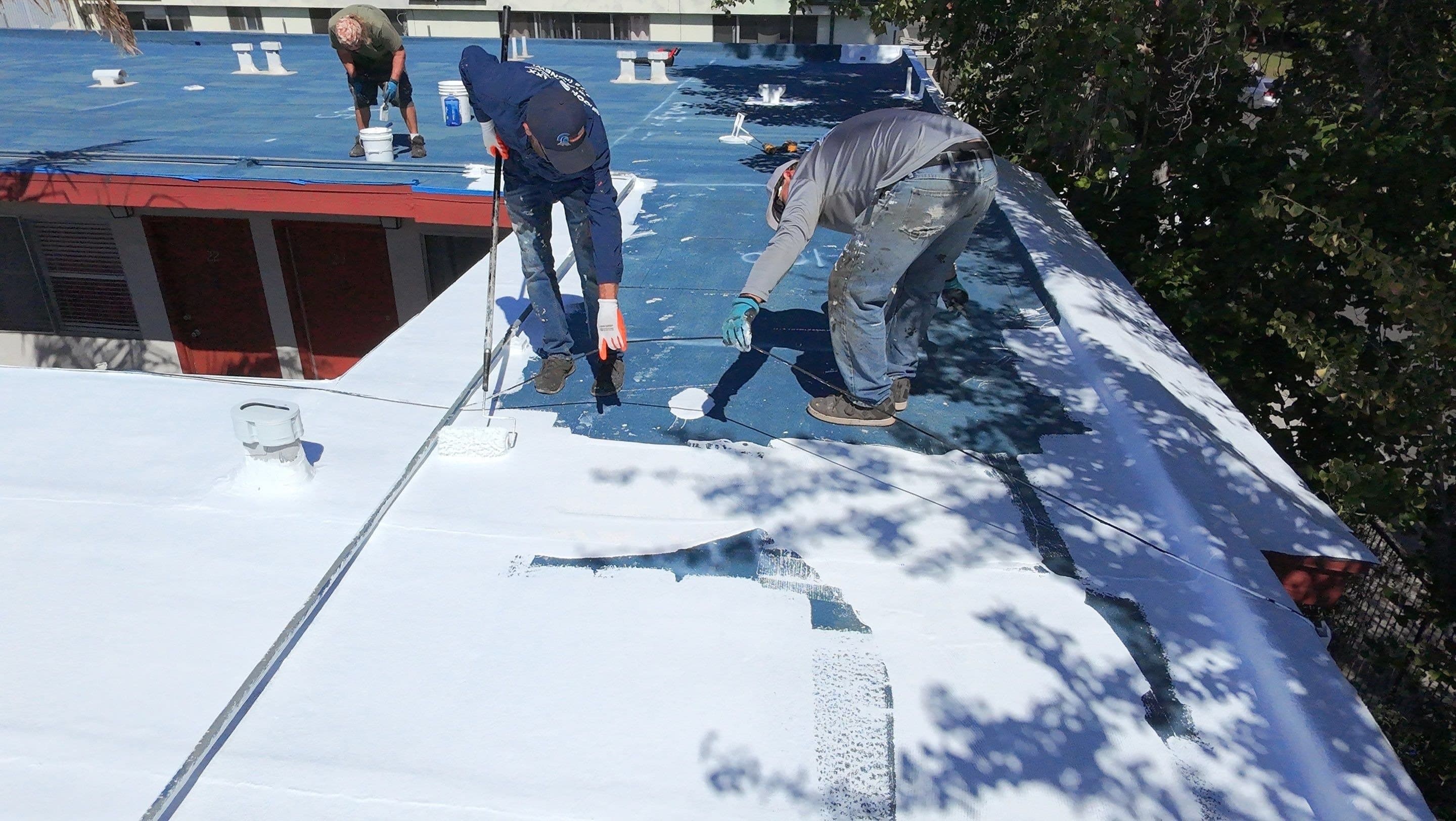 Two crew members rolling white silicone top coat over the blue base coat.