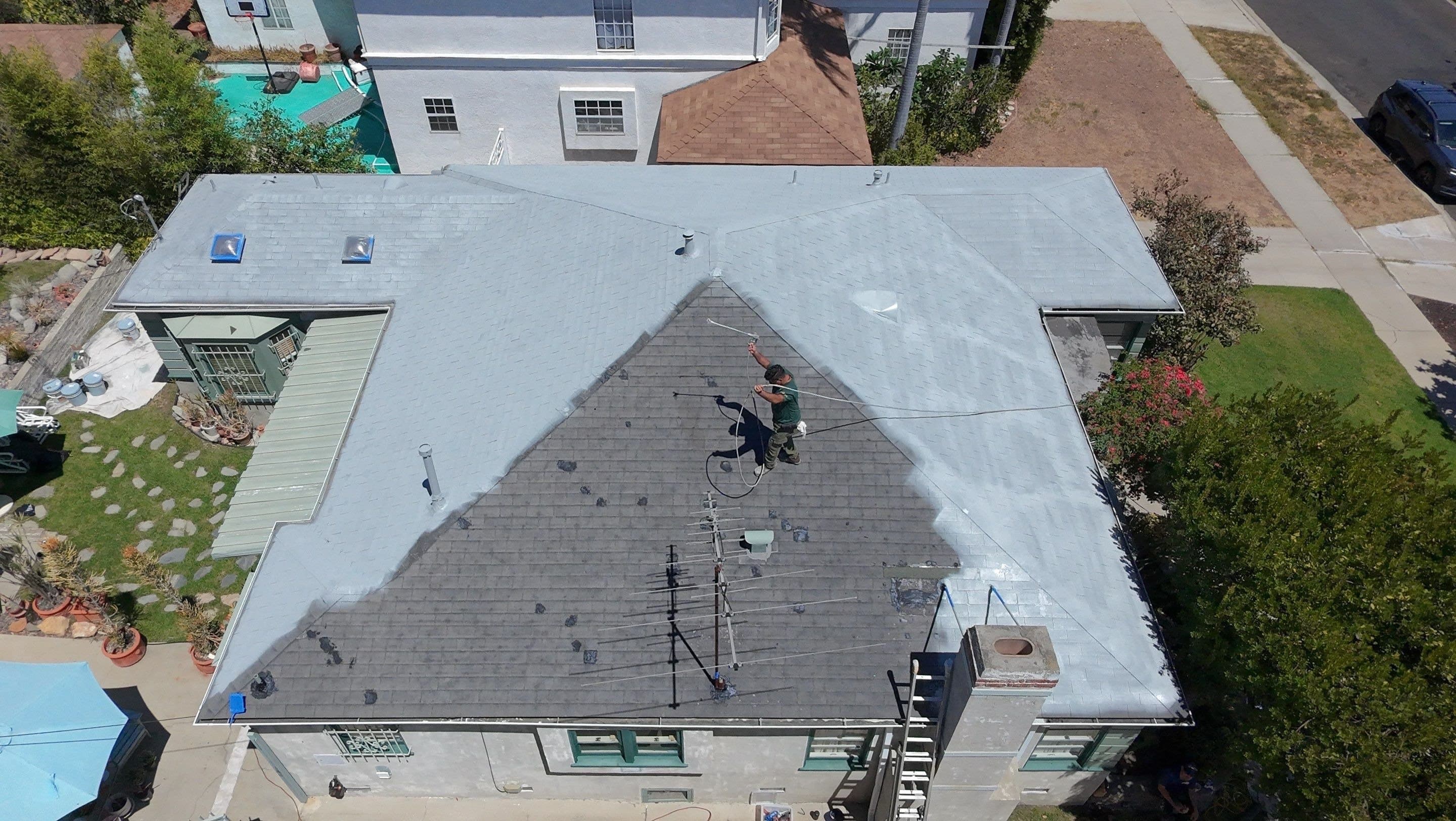 White coating halfway across the hip of a Los Angeles roof, with the untreated shingle still brown beside it.